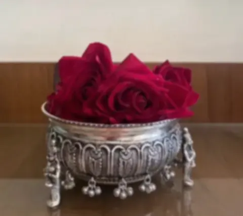 An antique silver urli filled with red roses