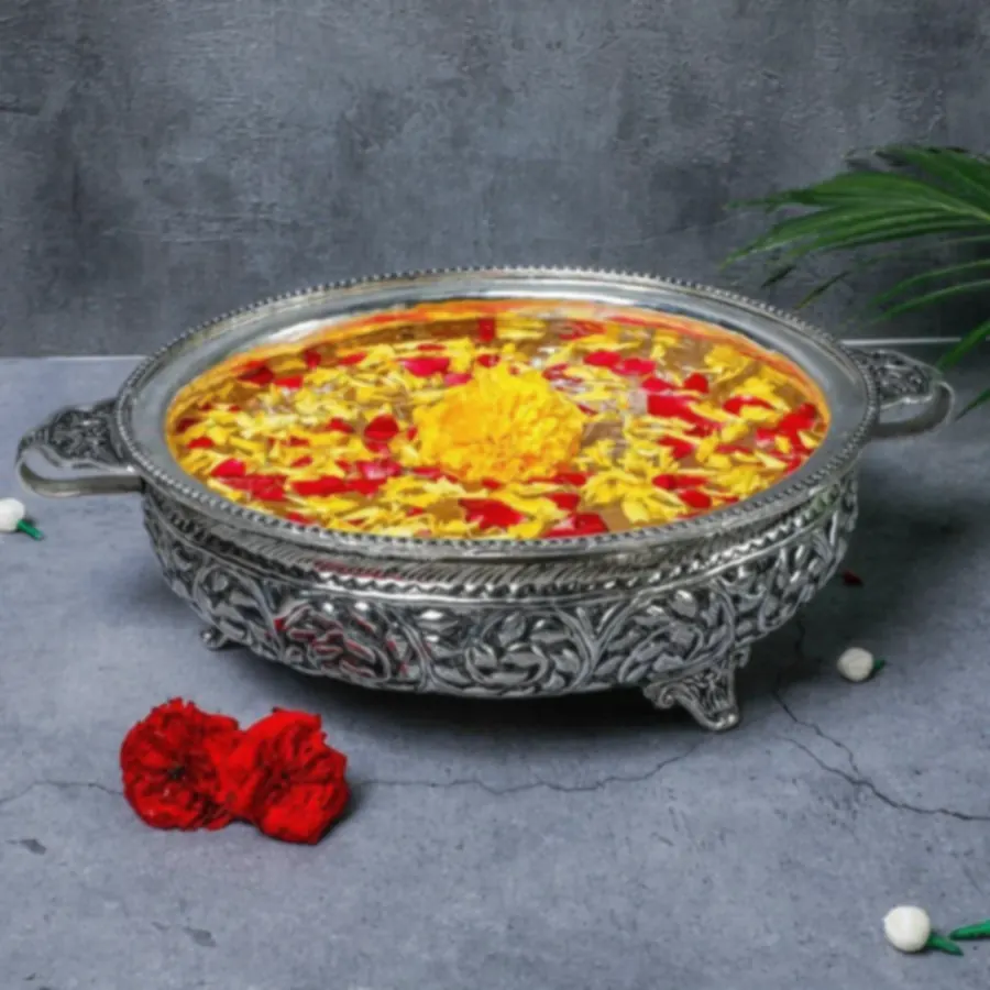 A wide antique-finish silver urli with marigolds and rose petals floating in water