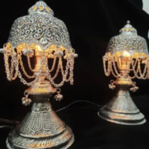 A pair of silver-plated table lamps with chandelier fringes, lit warmly