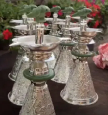 Silver diya stands with green stone rings and carved birds