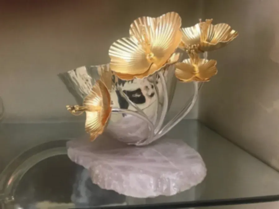 Gold-plated flowers rising from a silver bowl mounted on a slab of rose quartz