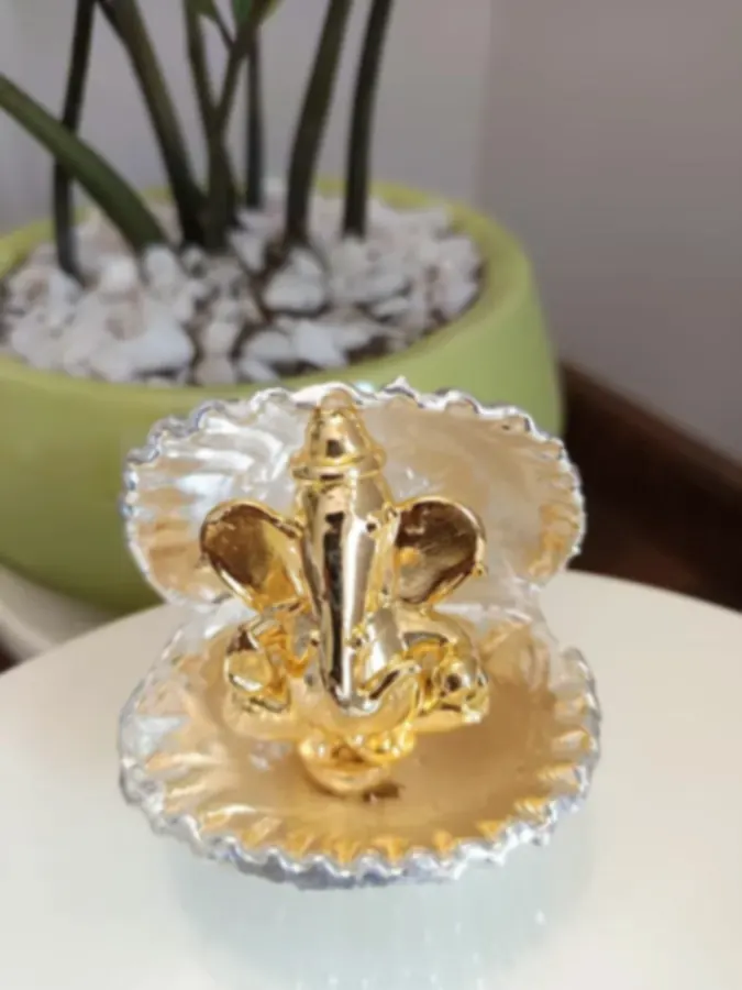 A small gold-plated Ganesh seated inside a silver-edged shell