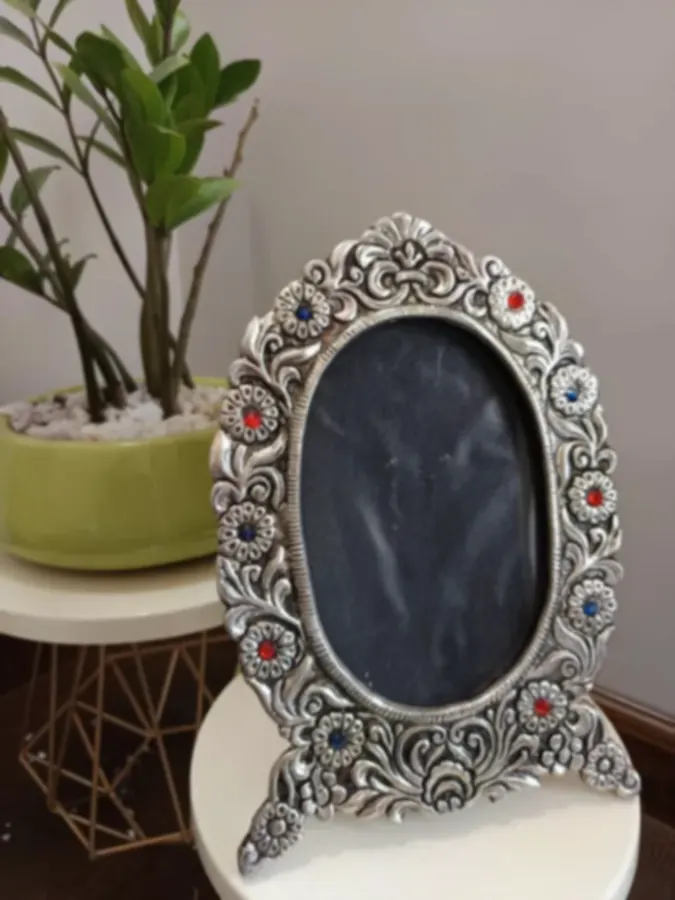 An oval silver-plated frame set with red and blue stones in a floral scroll