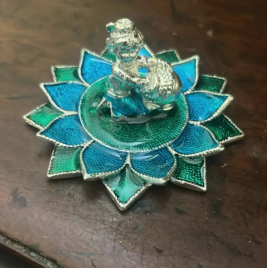 A silver Krishna figure on a lotus of blue and green enamel petals