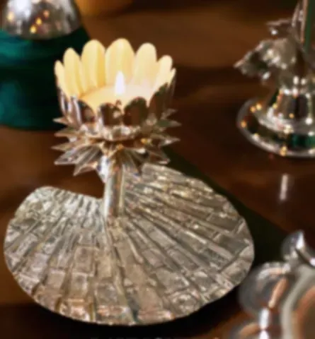 A silver-plated lotus tealight holder with a candle burning in it