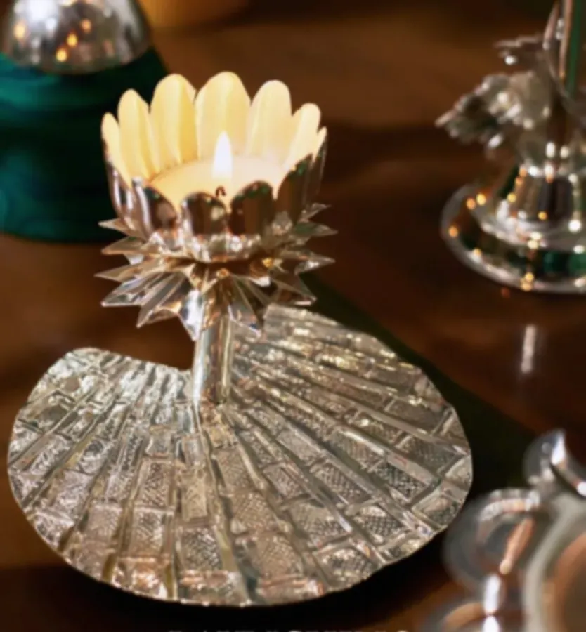 A silver-plated lotus tealight holder with a lit candle, petals catching the light