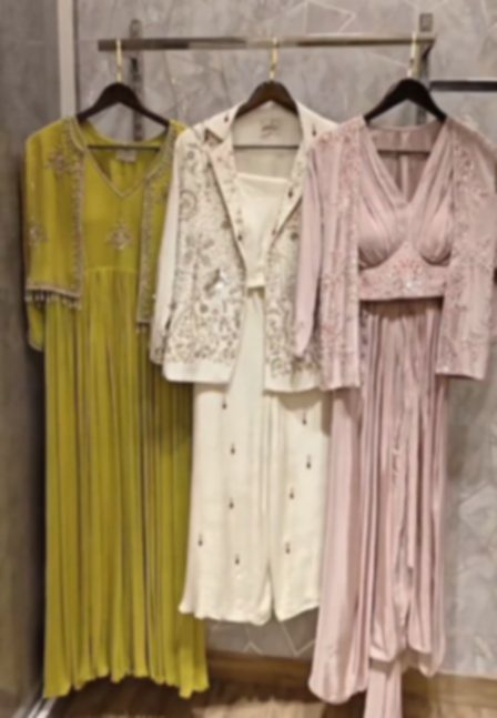 Three pieces hanging together: a pleated chartreuse kurta with beadwork at the yoke, an ivory jacket embroidered in silver over white trousers, and a blush pink draped set.