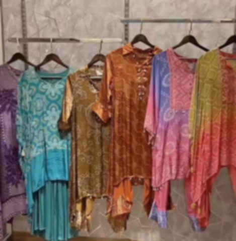 A run of tie-dyed pieces on a rail in teal, rust, olive, pink and purple, each printed in a different pattern.