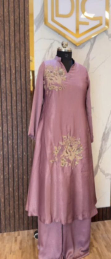 A mauve pink kurta and trousers on a mannequin with gold floral embroidery at the shoulder and on the skirt, beneath the boutique's gold monogram.