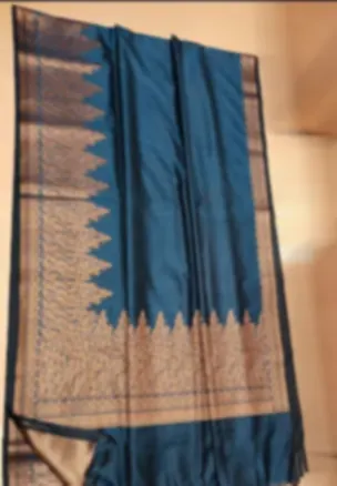 A teal Chanderi saree hanging in folds, with a fine gold brocade border along its length.