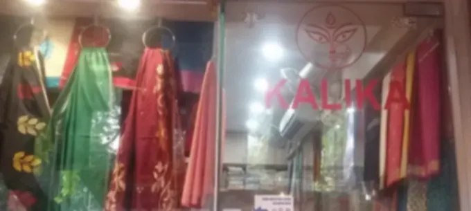 The shop window from the pavement: sarees in green, red and black hanging from rings above the doorway, with the name Brishtidhara on the glass.