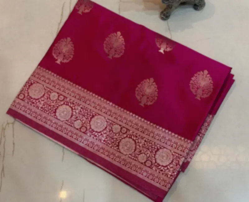 A crimson katan silk saree with silver zari motifs and a broad brocade border, beside a small brass figure of a bull.