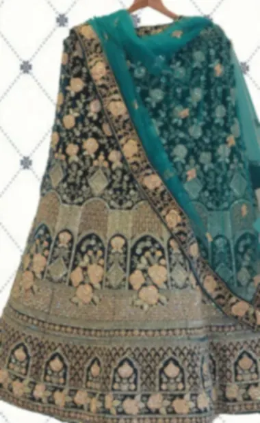 A deep teal bridal lehenga on a hanger, with gold zari arches on the skirt and a matching net dupatta.
