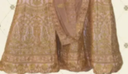 The lower skirt of a blush pink bridal lehenga, covered in heavy gold zari embroidery.