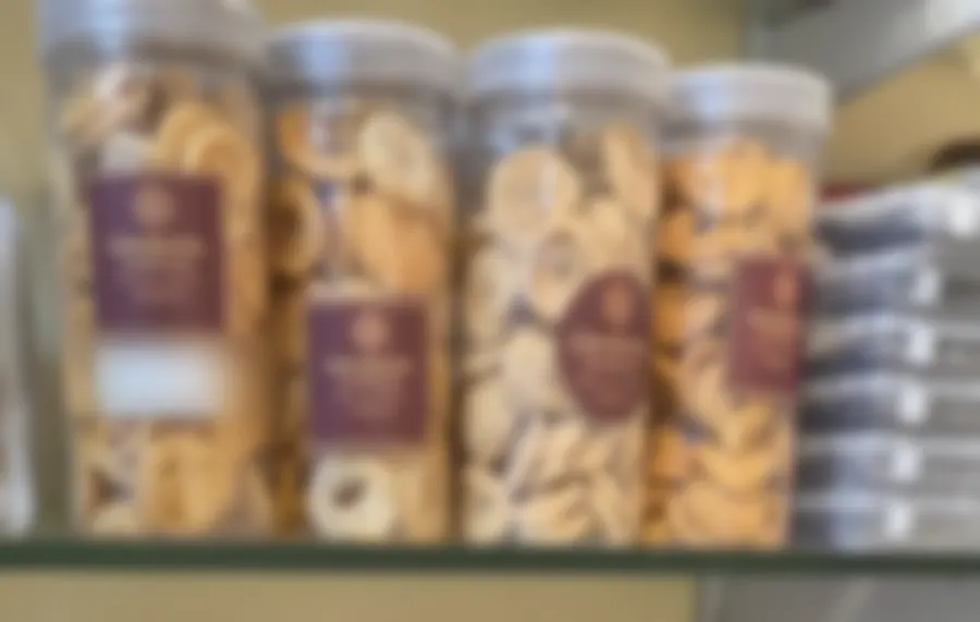 Four tall jars of golden murukku and chakli spirals on a glass shelf, each with the maroon Copperpot Namkeen House label