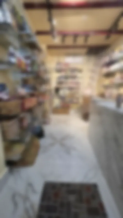 Inside Copperpot Namkeen House: a white marble floor and counter, glass shelves of snacks on both sides up to the ceiling, crimson rails and track lights above
