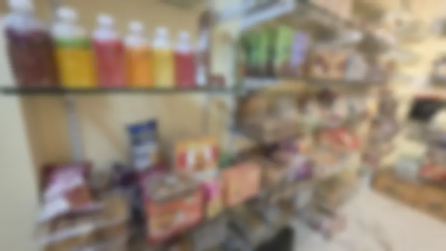 A glass shelf of fruit drinks in bright bottles, boxes of cookies and bags of vegetable chips