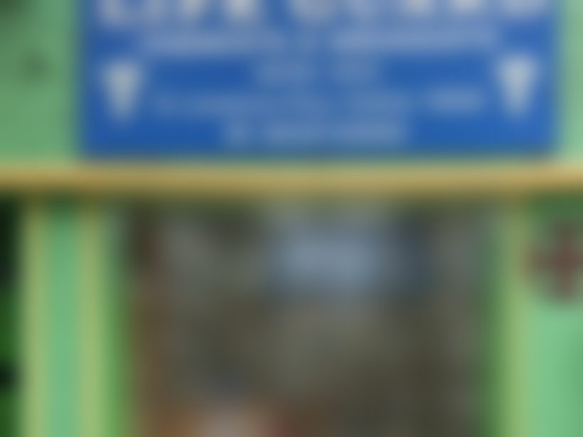 The blue Larkspur signboard close up, above the open shopfront and its glass-fronted cabinets of medicine.