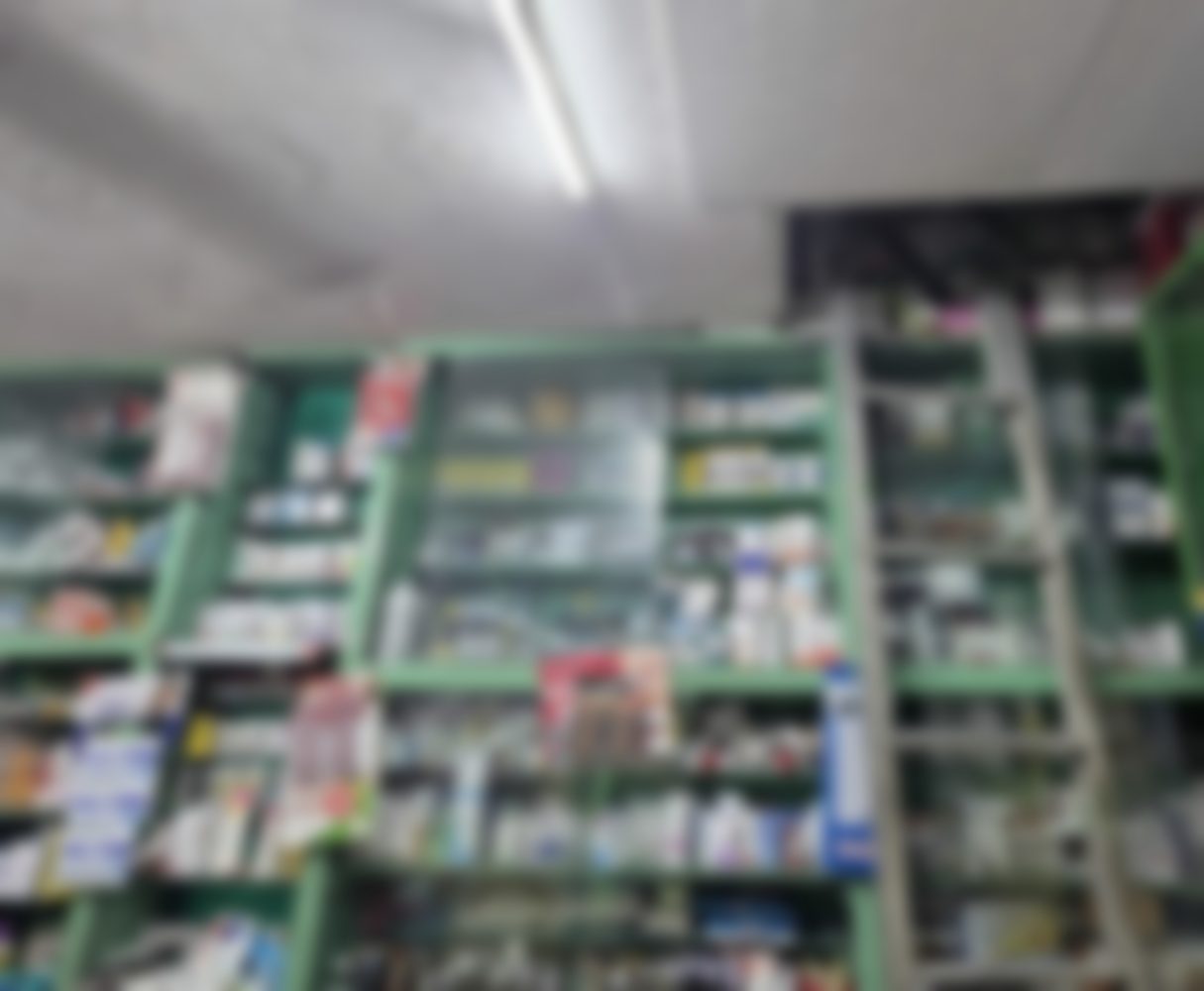The dispensary wall inside Larkspur: glazed green wooden cabinets stocked from floor to ceiling with boxed and bottled medicines, an aluminium ladder resting against them.