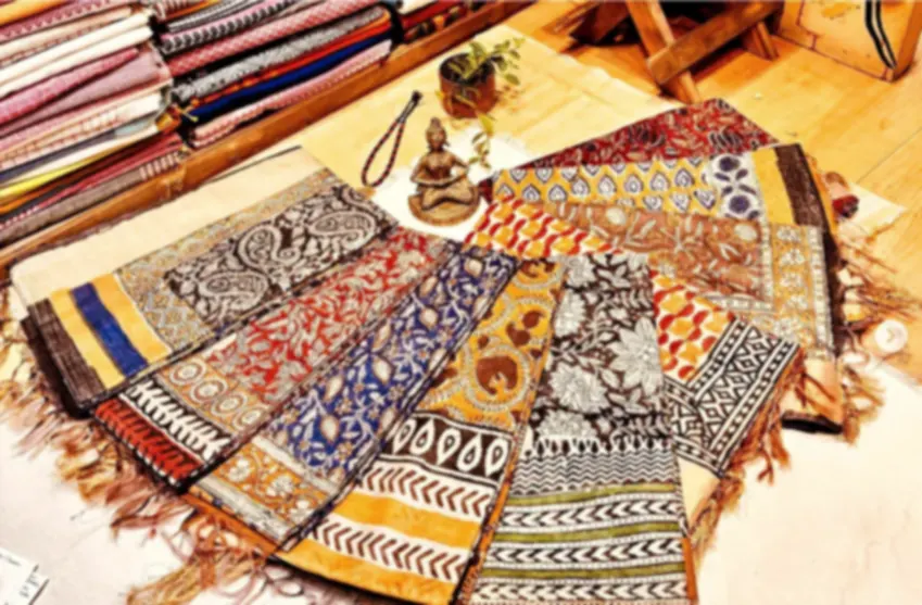 Several blended tussar dupattas in patterned block prints, fanned out on a wooden floor.