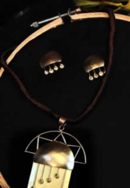 A hand-cut brass and copper necklace and earring set with geometric shapes, on a dark ground.