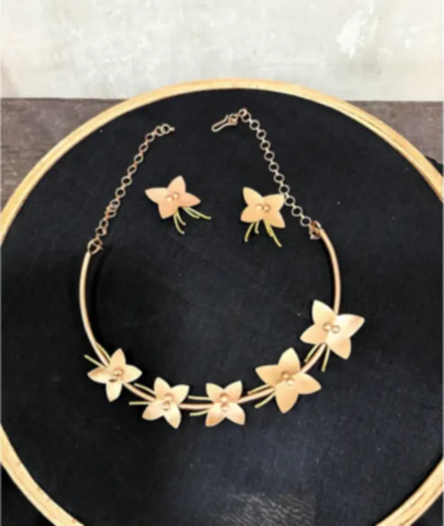 A brass necklace and earring set with hand-cut floral silhouettes, laid on a dark ground in a hoop.