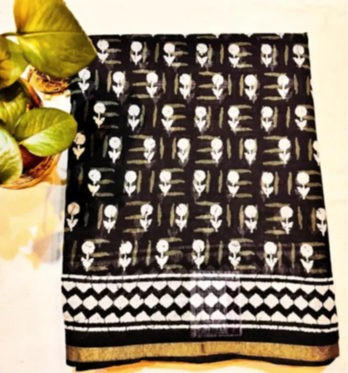 A black Chanderi saree printed with white motifs and a geometric border, folded on a wooden surface.