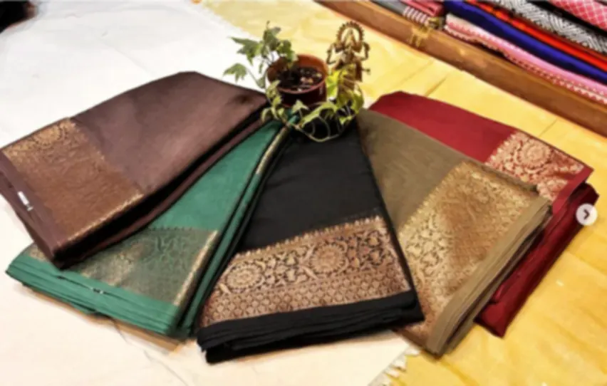 Four Chanderi sarees in brown, green, black and maroon, folded and fanned to show their zari borders.