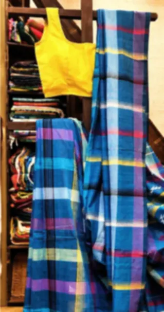A blue and pink checked Fulia cotton saree with coloured tassels, hanging in the shop with a yellow blouse.
