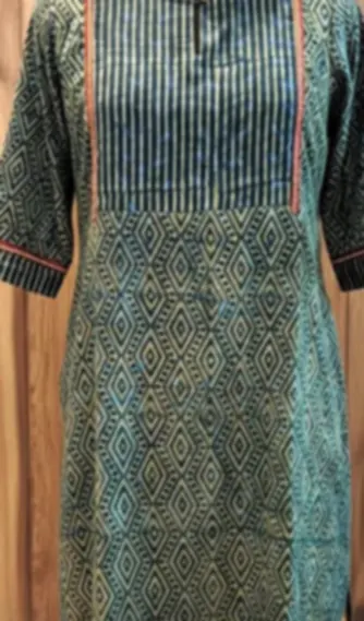 A green cotton kurti with an ikat-style print and contrast piping, on a mannequin.