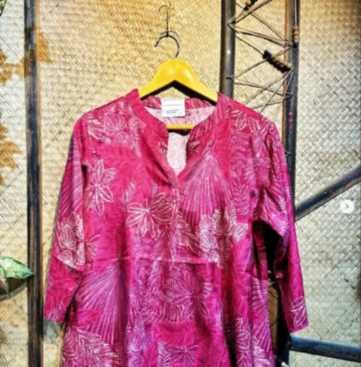 A pink shibori patterned cotton kurti with white floral bursts, on a hanger against a woven backdrop.