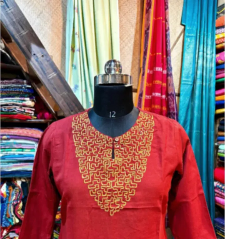 A red cotton kurti with gold thread embroidery at the neckline, on a mannequin in the shop.