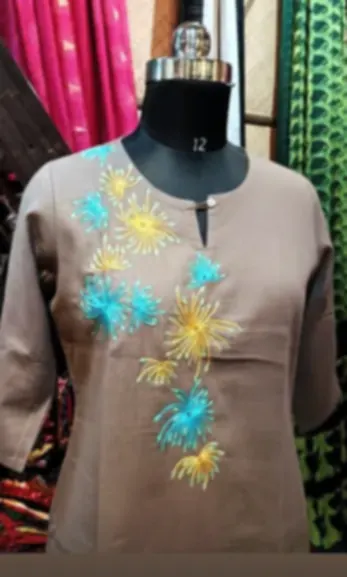 A taupe cotton kurti with turquoise and yellow hand embroidery at the neckline, on a mannequin.