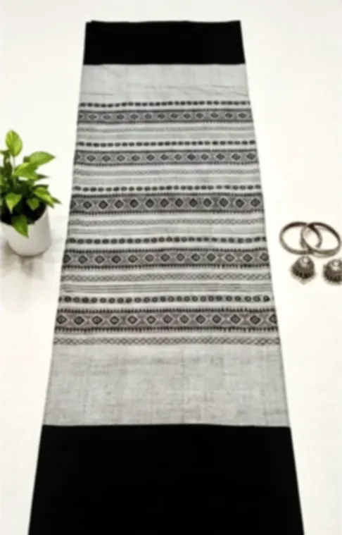 A grey and black Dhonekhali cotton saree with fine woven stripes, folded lengthways beside silver bangles.