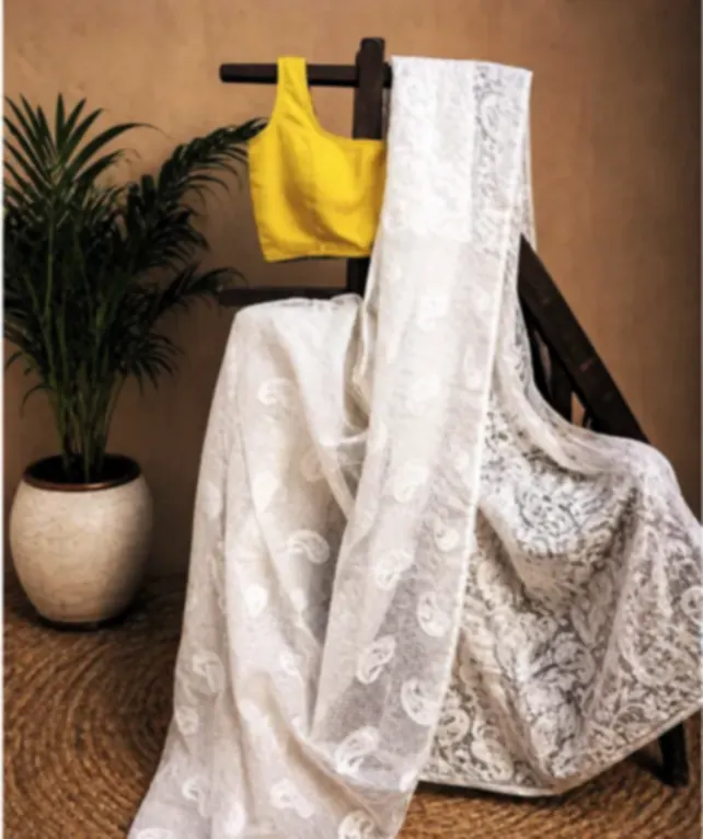 An off-white Fulia reshm saree with fine machine embroidery, draped over a wooden rack beside a yellow blouse.