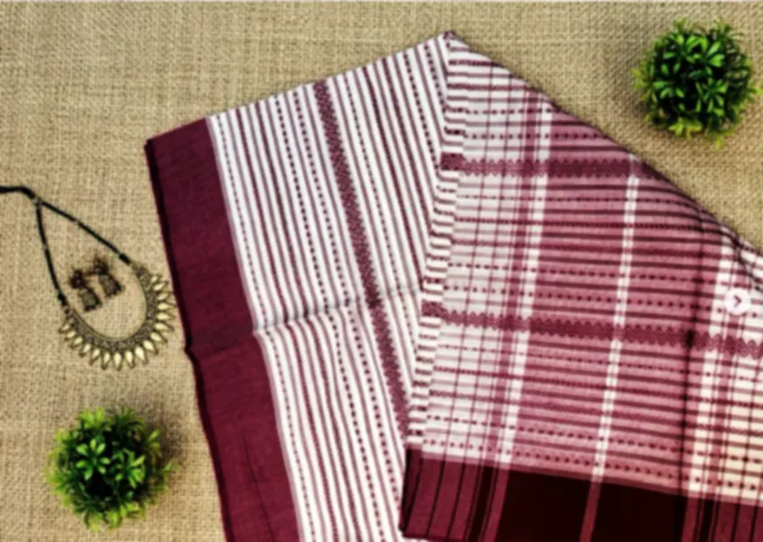 A maroon and white checked handloom cotton saree folded on jute, with a beaded necklace beside it.