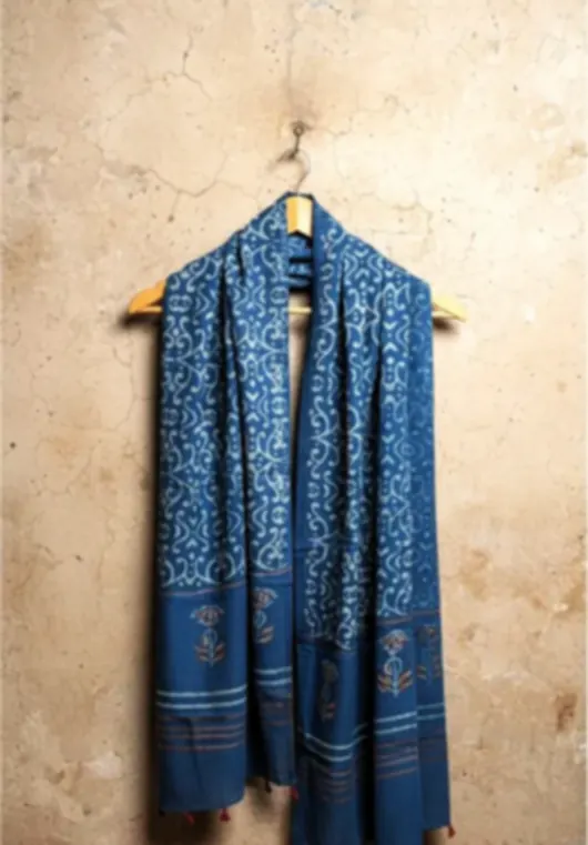 An indigo block printed cotton stole hanging on a wooden peg against a pale stone wall.