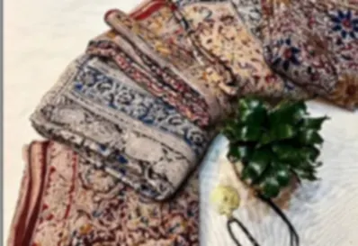Several Kalamkari cotton sarees in earthy tones, folded and fanned out with a cord necklace.