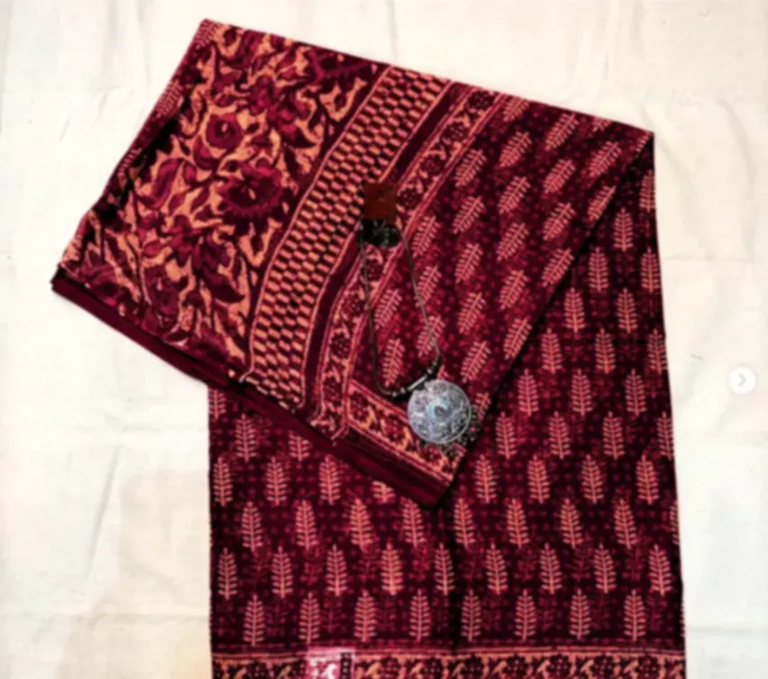 A deep red Kota cotton saree printed all over with small leaf motifs and a patterned border.