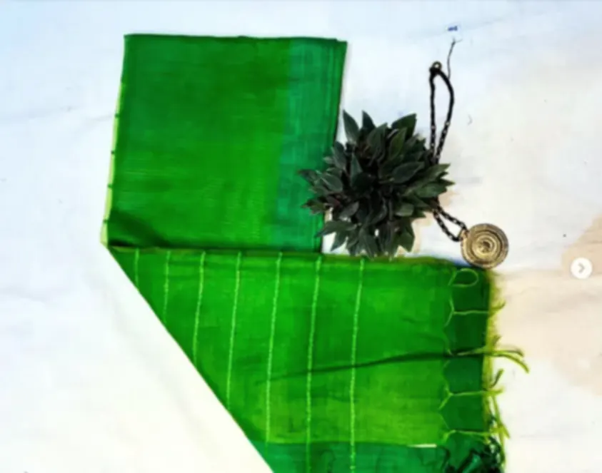 A bright green Matka blended silk saree with fine woven stripes, folded on white cloth with a pendant.