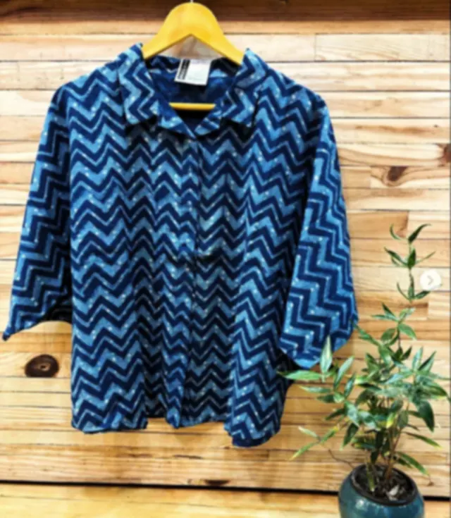 An indigo Dabu printed khadi cotton shirt with a chevron pattern, hanging against a wooden wall.