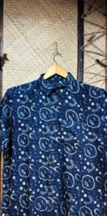 An indigo handwoven cotton shirt with a white block printed pattern, on a hanger against jute.