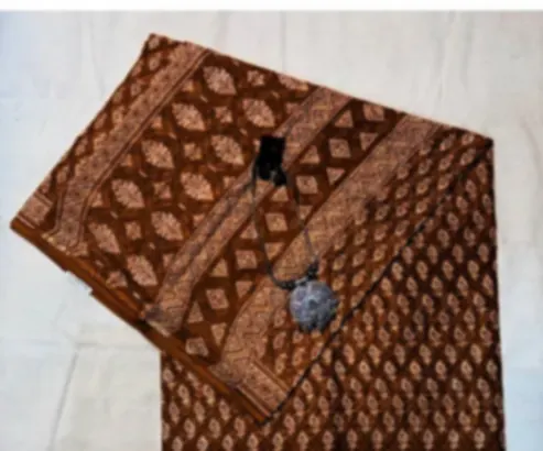 An ochre mulmul saree block printed with small motifs and a patterned border, folded on cream cloth.