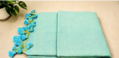 A fresh aqua mulmul saree folded on cream cloth with playful blue and yellow tassels.