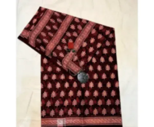 A brick red mulmul saree with repeating botanical motifs and a printed border, folded on cream cloth.