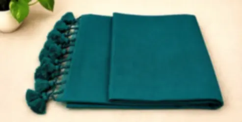 A deep teal mulmul saree folded on cream cloth with tonal teal tassels.