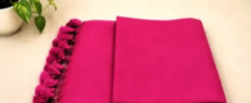 A bright fuchsia mulmul saree folded on cream cloth with matching pink tassels.