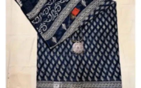 A deep indigo mulmul saree printed with a vine border and small motifs, folded on cream cloth.