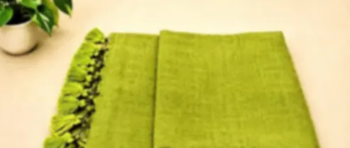 An earthy moss green mulmul saree with visible woven texture, folded on cream cloth with green tassels.