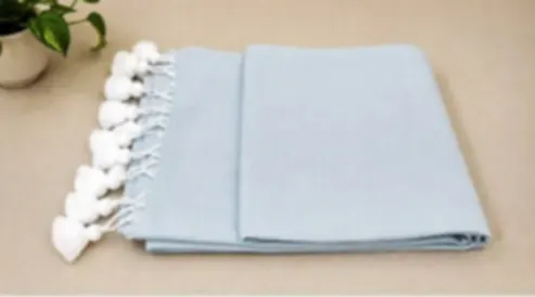 A pale powder blue mulmul saree folded on cream cloth with white tassels.